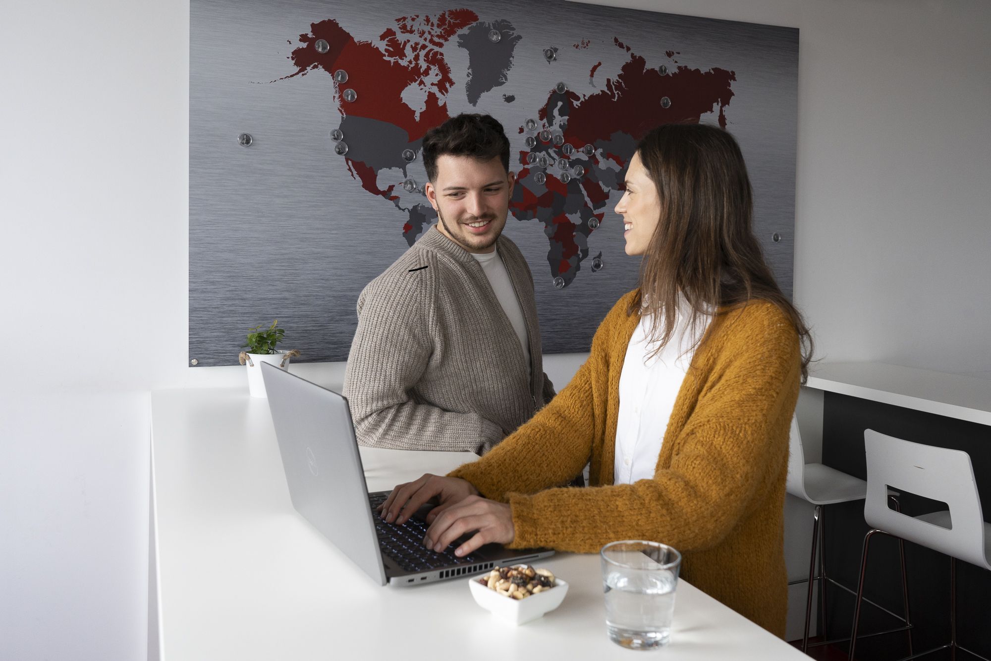 A young man and woman discussing a project. The woman is working on a laptop.